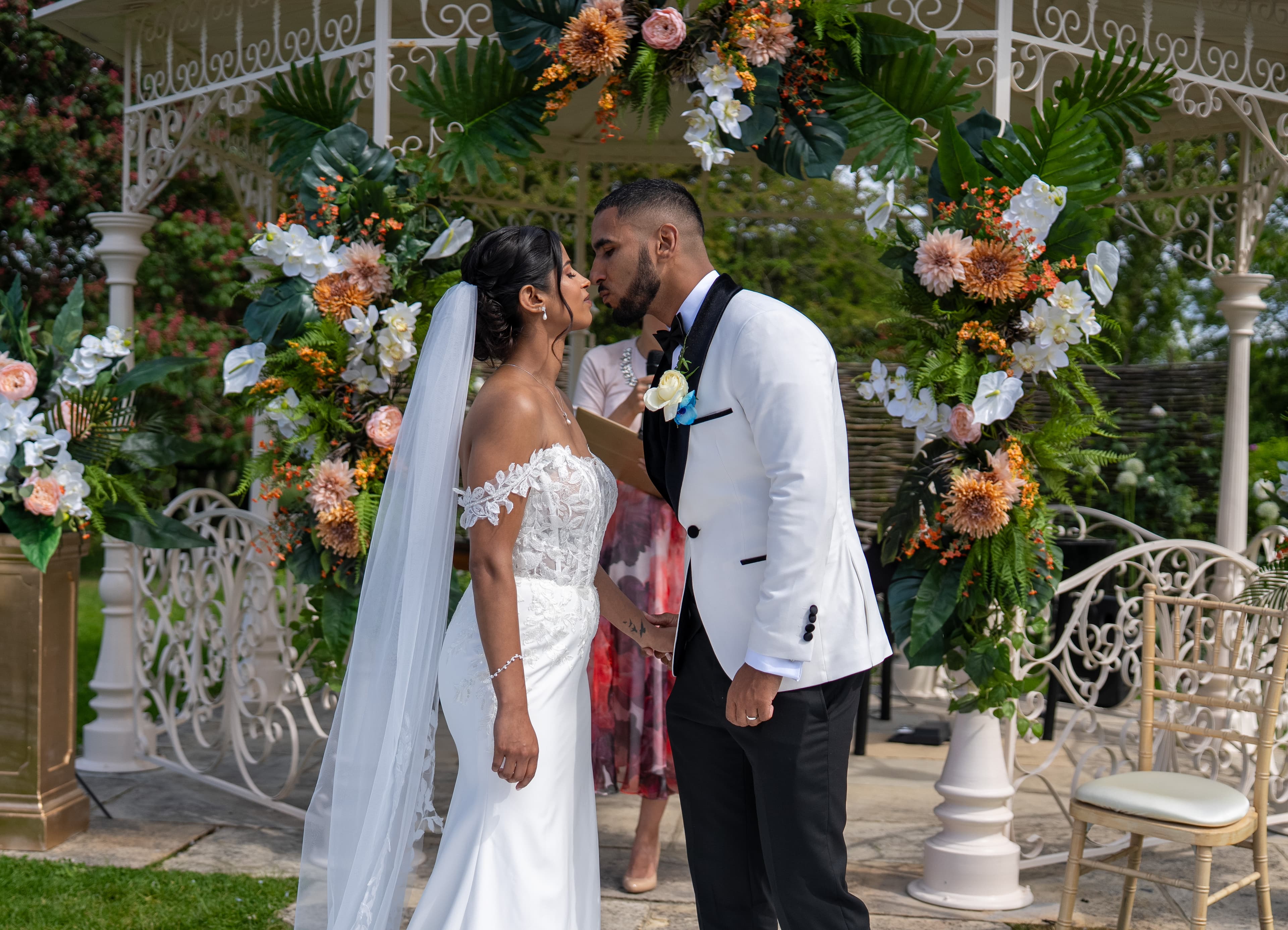 A newly married couple kiss beneath floral ceremony decorations.